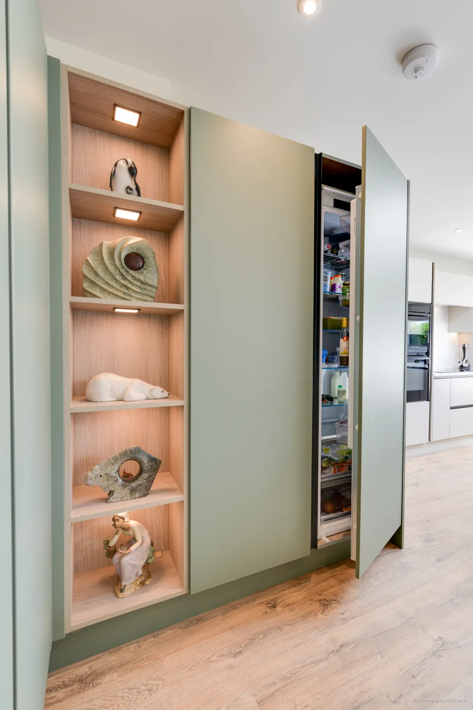 Lit oak shelves in a reed green tall unit, ornaments on the shelves.