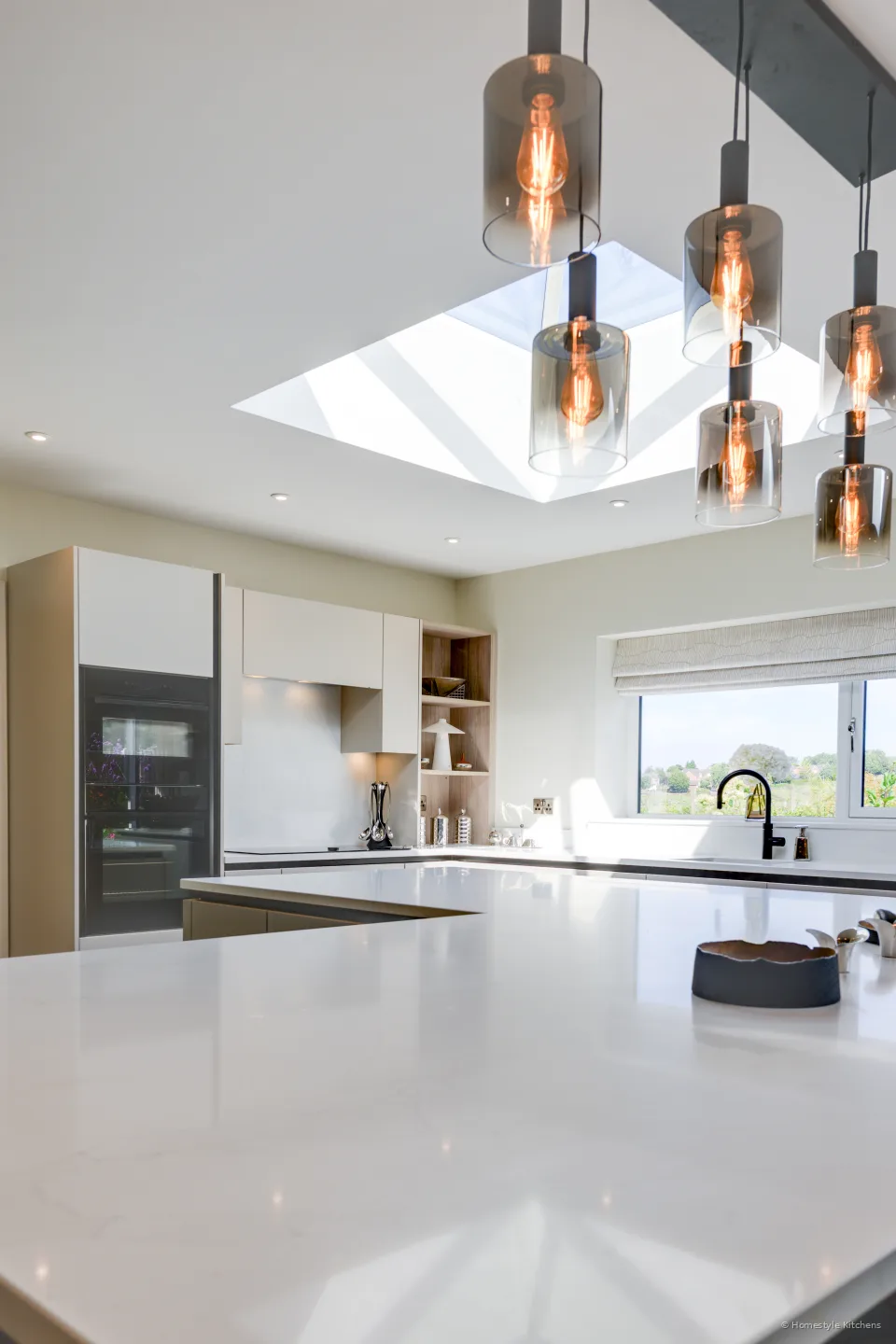 Island worktop with a black hob, pendants and window light.