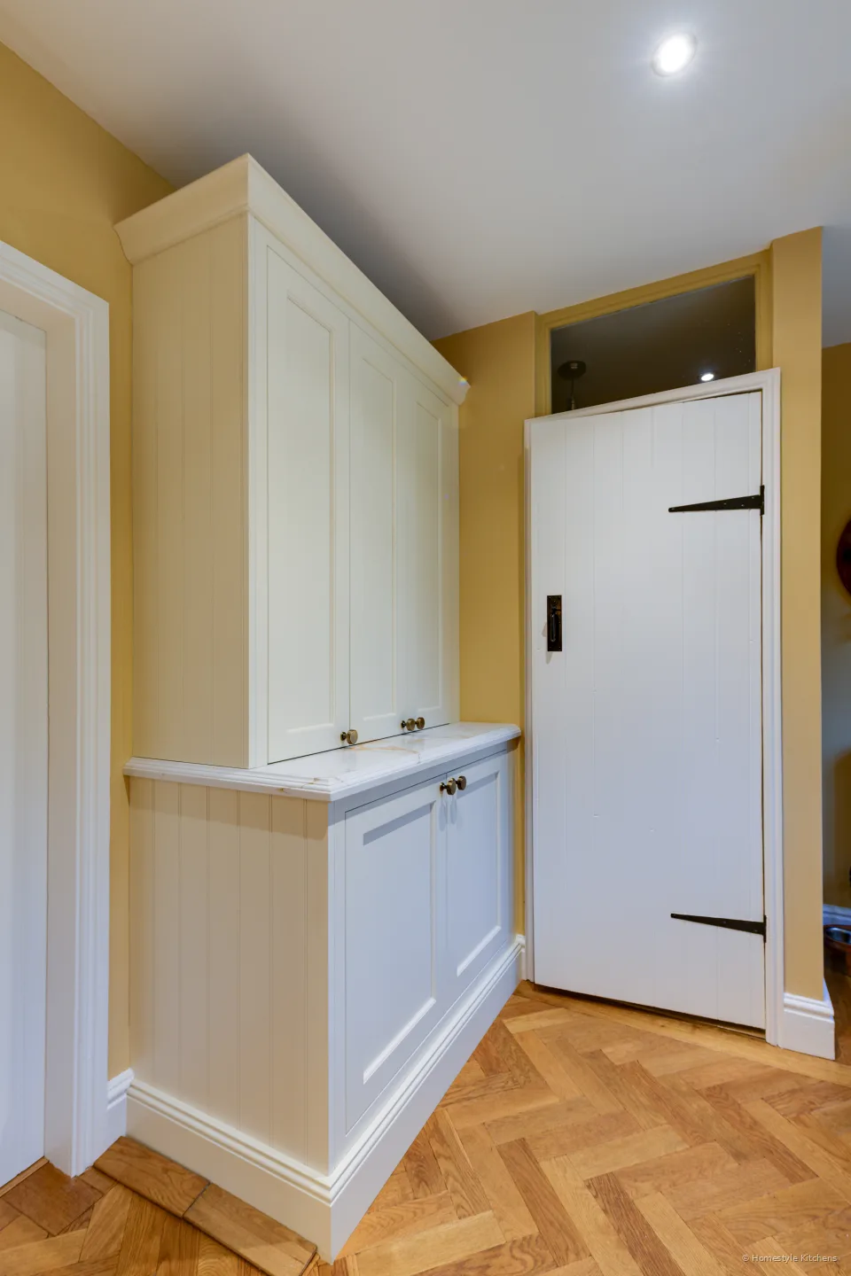 Cream painted dresser cabinet with a stone shelf, next to a boarded door with black iron hinges.