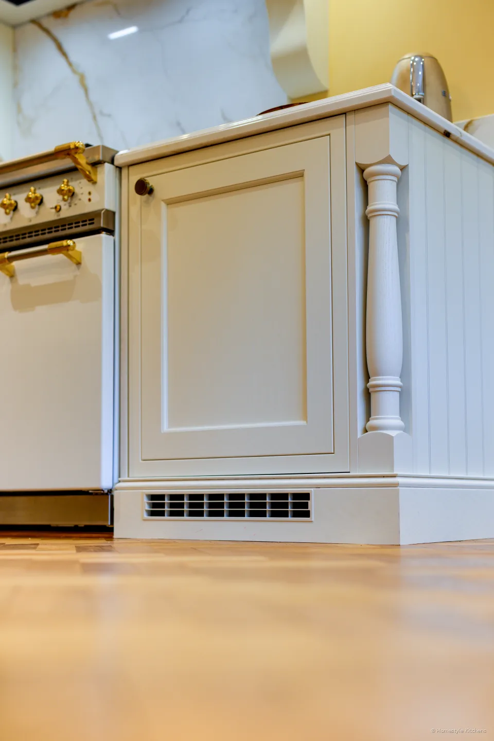 Cream painted cabinet end with a turned post, plinth vent and herringbone floor.