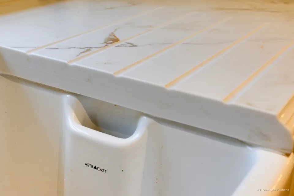 Drainer grooves cut into Chicstone Calacatta Gold quartz beside a white ceramic sink.