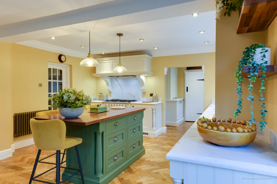 Cream painted kitchen and green island with oak top, seen from the doorway, pendants over the island.