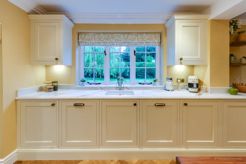 Cream painted kitchen run under a window, Calacatta Gold quartz worktop, brass bridge tap and ceramic sink.