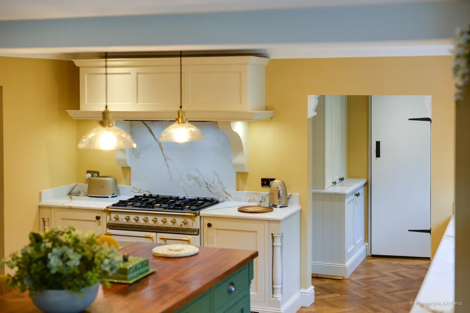 Looking across a green oak-topped island to a cream painted range wall and Calacatta Gold splashback.