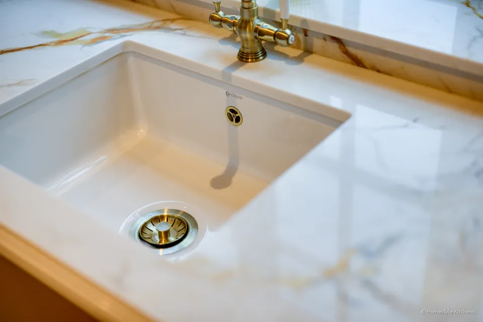 White ceramic undermount sink in Chicstone Calacatta Gold quartz, brass waste and overflow.