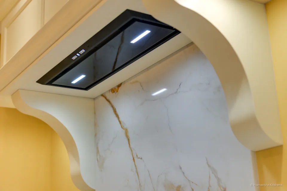 Black Luxair canopy extractor fitted inside a cream painted mantel hood, Calacatta Gold splashback below.
