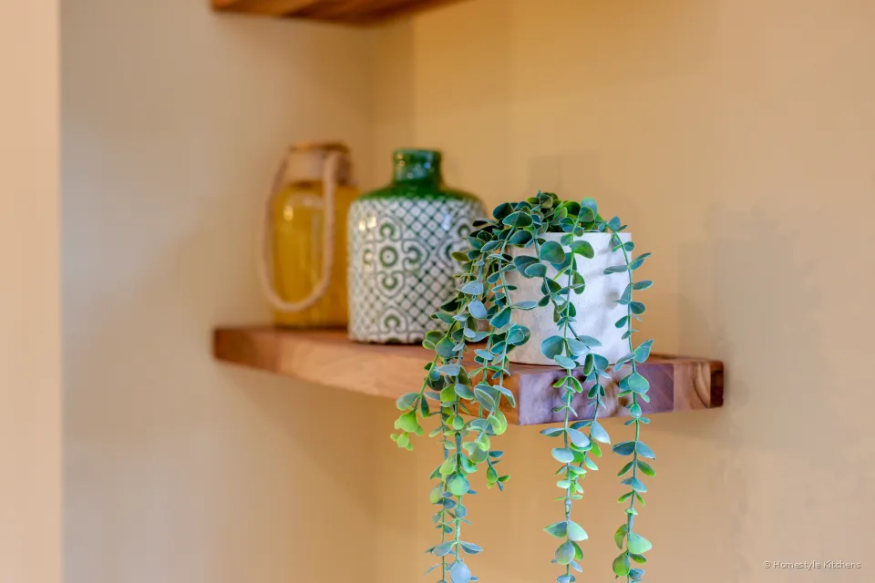 Oak floating shelf with a trailing plant and ceramics, cream painted cabinet below.