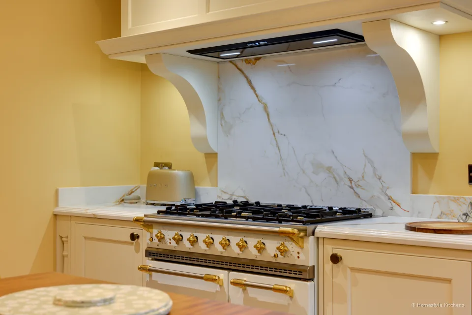 Cream range and mantel with brass knobs, extractor lights in the canopy and Calacatta Gold splashback.