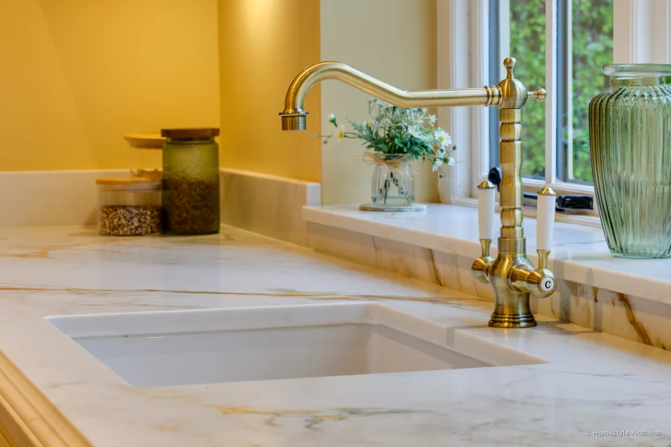 Brass bridge tap over a white ceramic undermount sink in Chicstone Calacatta Gold quartz.