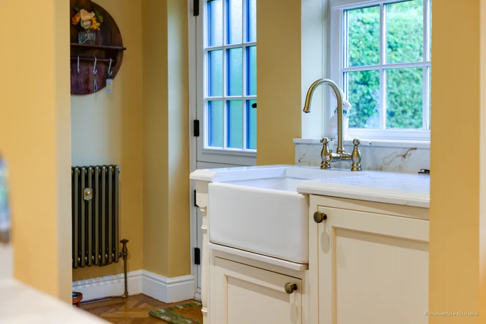 White ceramic butler sink and brass bridge tap on Calacatta Gold quartz, cream cabinets and herringbone floor.
