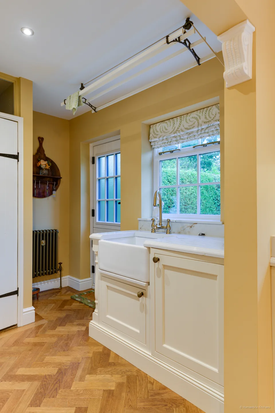 Cream painted utility with a ceramic butler sink, brass bridge tap, Calacatta Gold worktop and a drying rack.