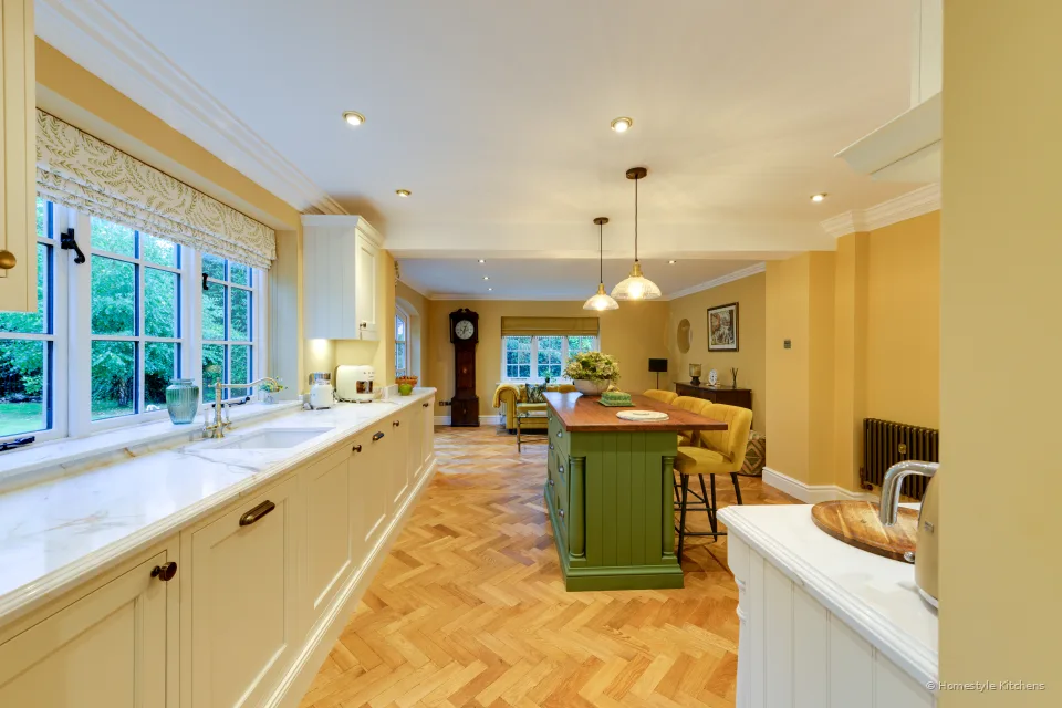 Long cream painted kitchen run under a window, Calacatta Gold worktop, green island and herringbone floor.
