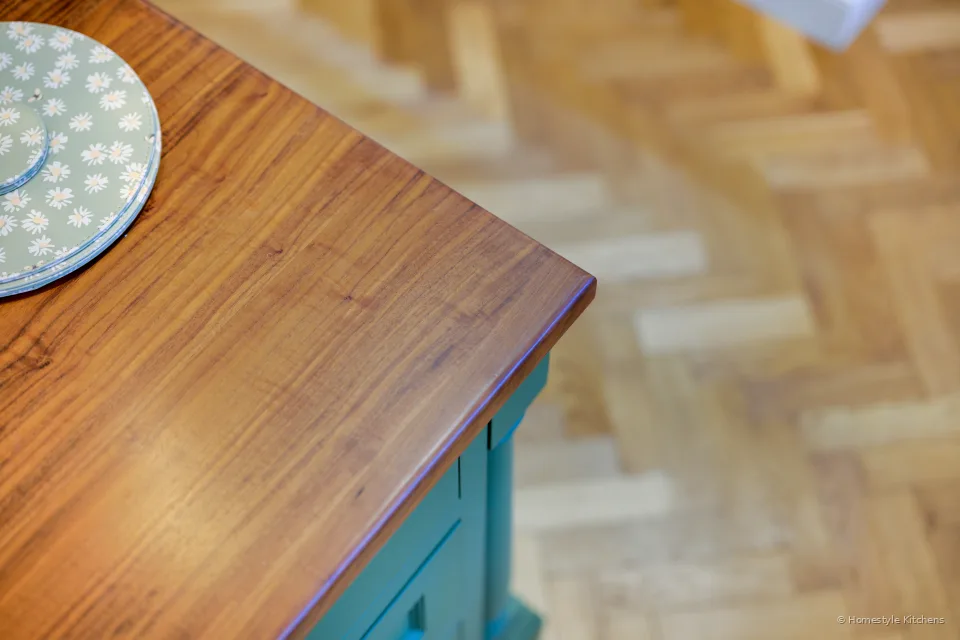 Oak island worktop corner with a stack of plates, herringbone floor below.