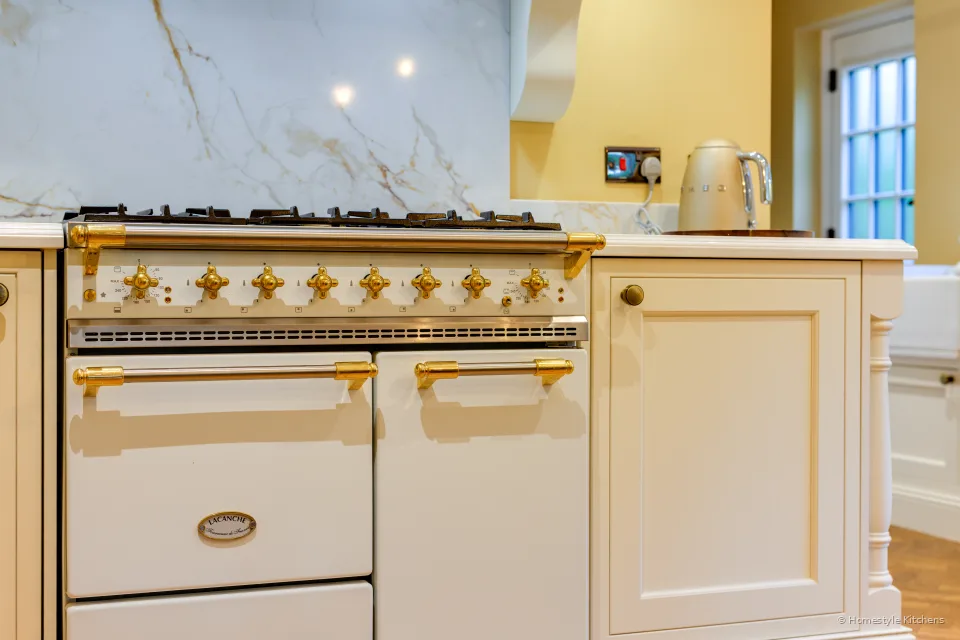 Cream range cooker with brass knobs, Calacatta Gold splashback and cream painted cabinets either side.
