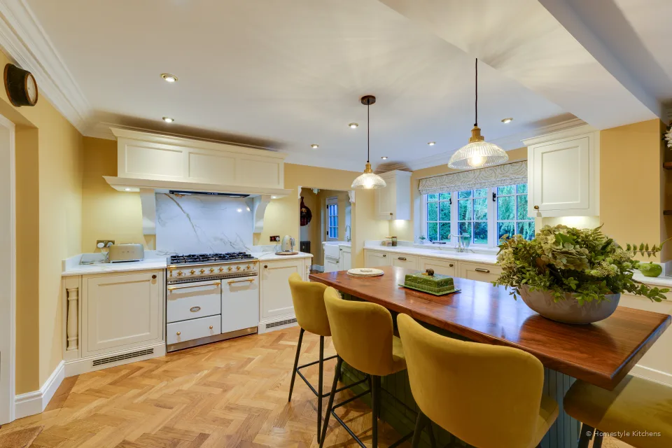 Kitchen with cream painted cabinets, Calacatta Gold worktops, a range under a canopy, and a green island with an oak top.
