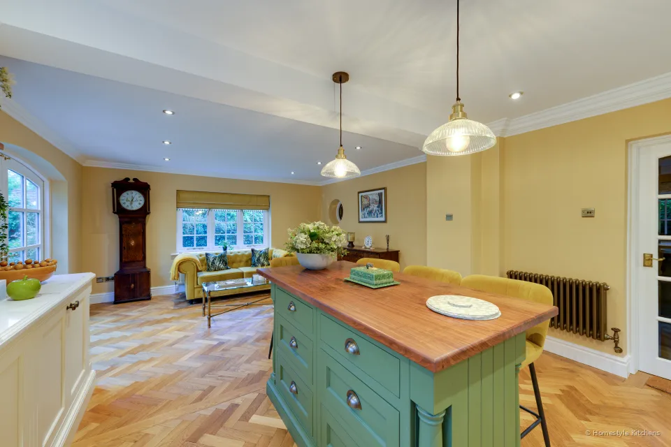 Open-plan kitchen with cream cabinets, a green island with an oak top, and a seating area beyond.
