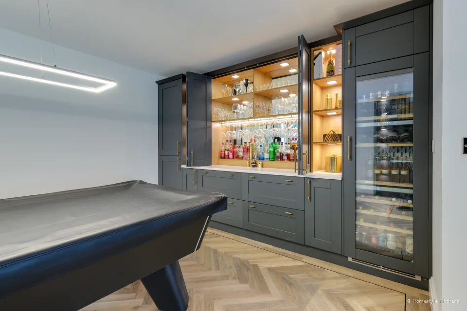 Lit oak bar shelving with bottles and a glass-fronted drinks fridge.