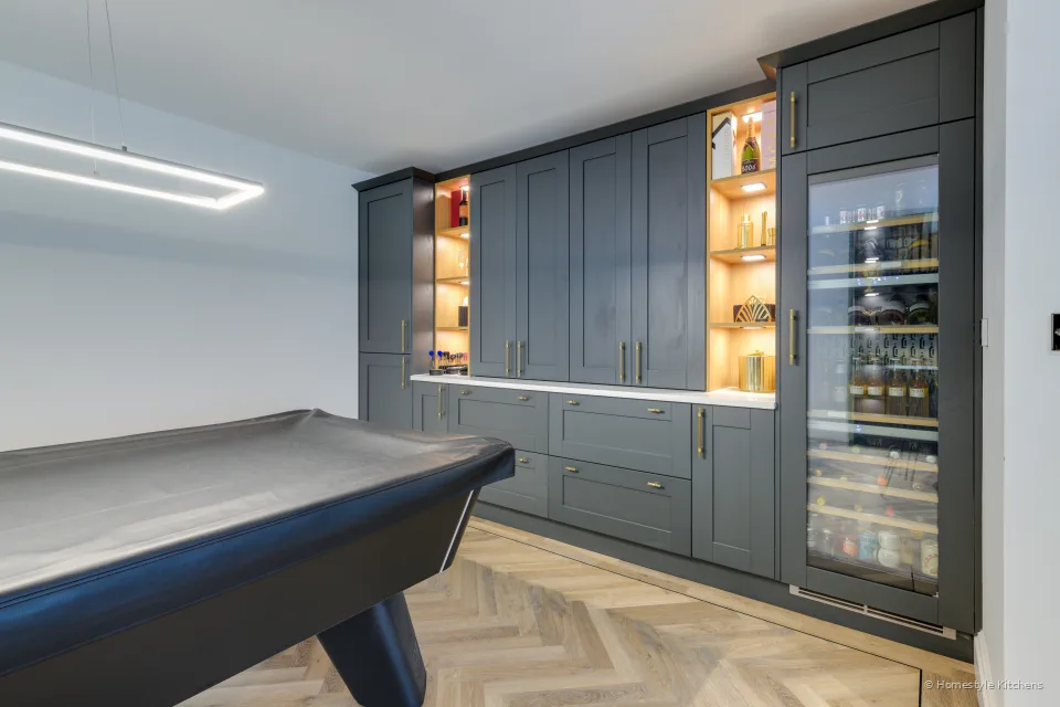Dark blue-grey shaker bar run and oak-lined lit shelving, pool table in front.