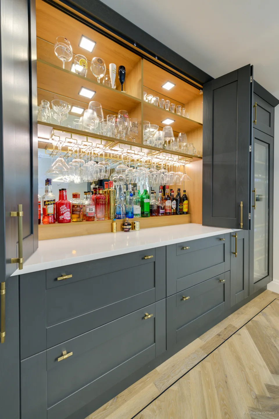 Glassware on lit oak shelving above a white bar worktop.