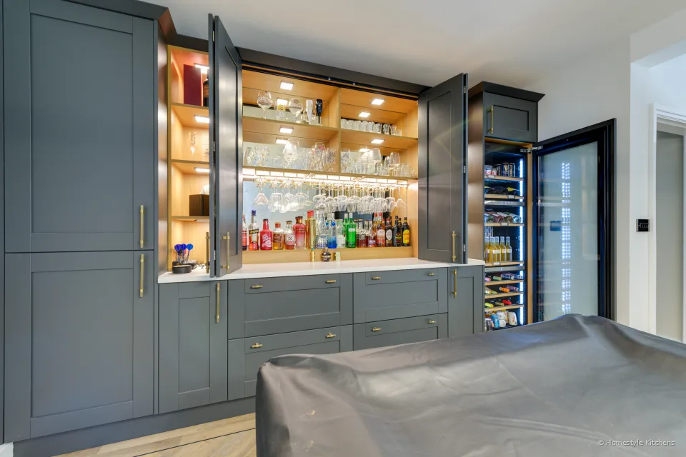 Dark blue-grey shaker bar with open lit oak shelves and brass handles.