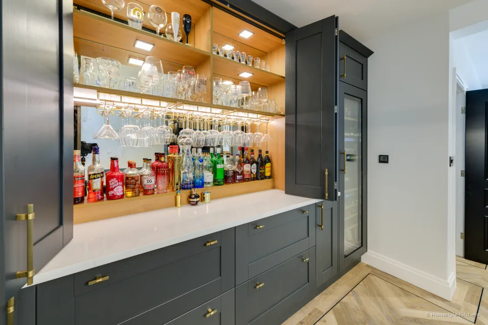 White worktop bar with spirits on lit oak shelves and a brass rail.