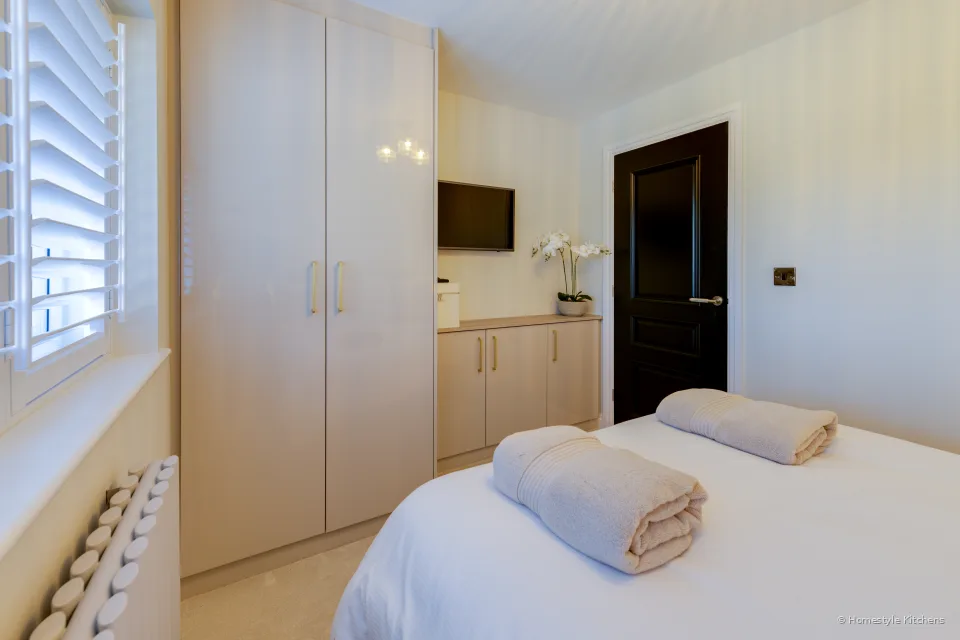 Pale gloss fitted wardrobes and a wall-mounted TV beside the bed.