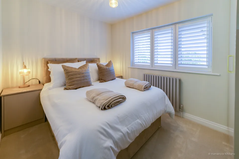 Bedroom with an upholstered headboard, shuttered window and pale fitted units.