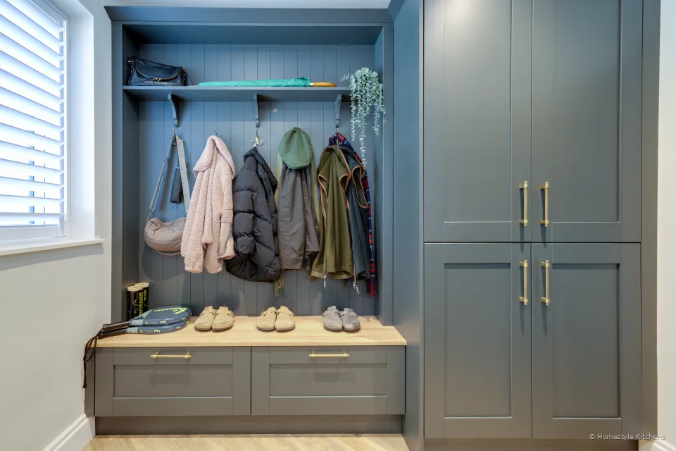 Grey-blue shaker boot room with an oak bench, coat hooks and brass handles.