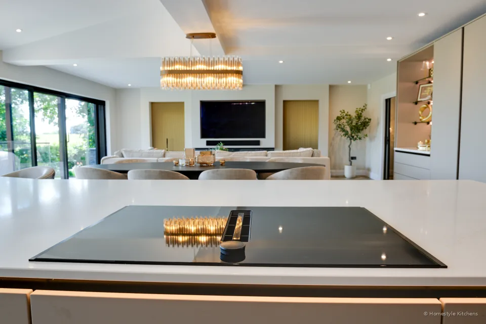 Black vented induction hob in white quartz, open-plan living beyond.