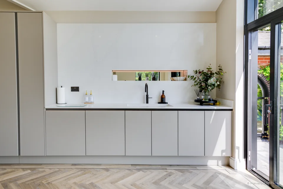 Pale tall units and appliance housing, quartz worktop in front.