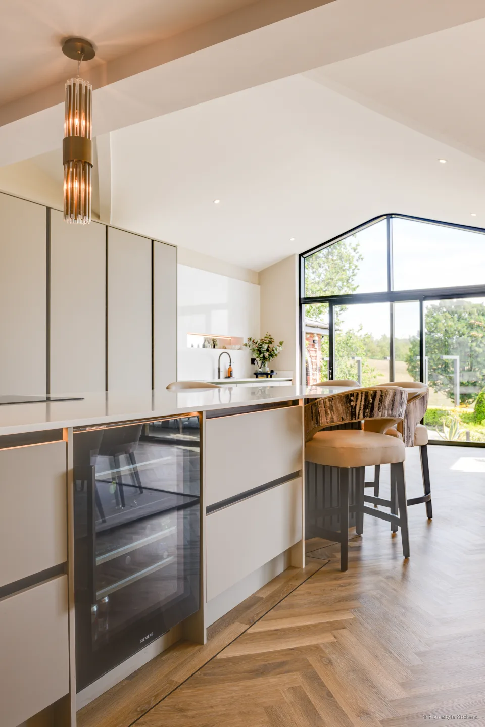 Closed run of tall pale handleless units, herringbone oak floor.
