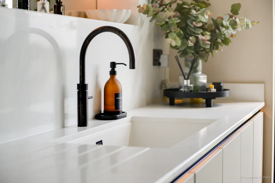 White undermount sink and matt black tap in white quartz, pale handleless units.