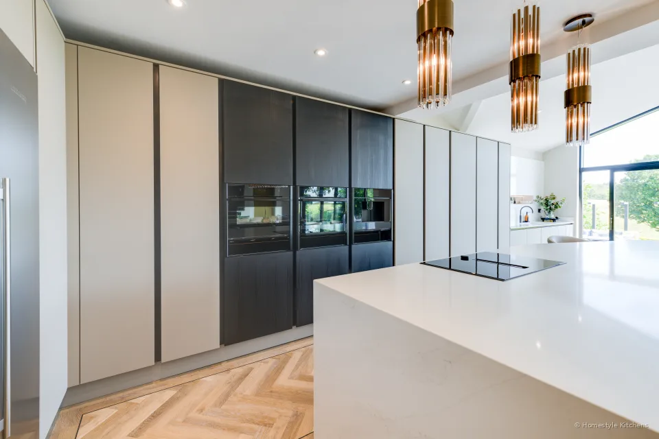 Pale grey island with brass pendants, dark tall run and glazing behind.
