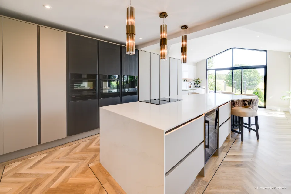 Open-plan kitchen with a pale grey island, dark tall units, white quartz and herringbone oak.