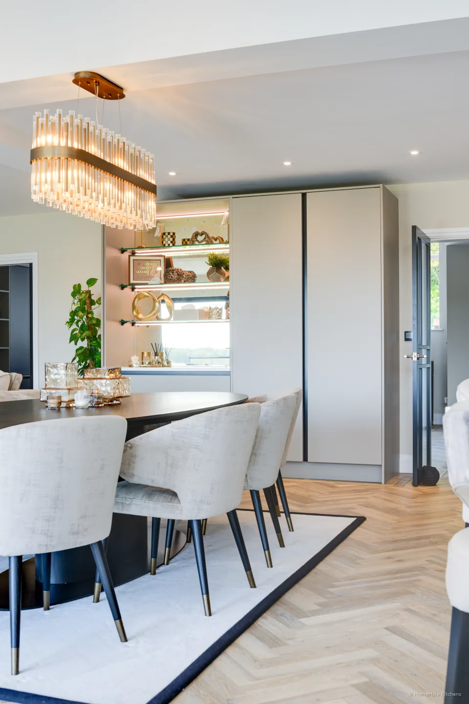 Dining chairs at a round table, tall pale kitchen units behind.