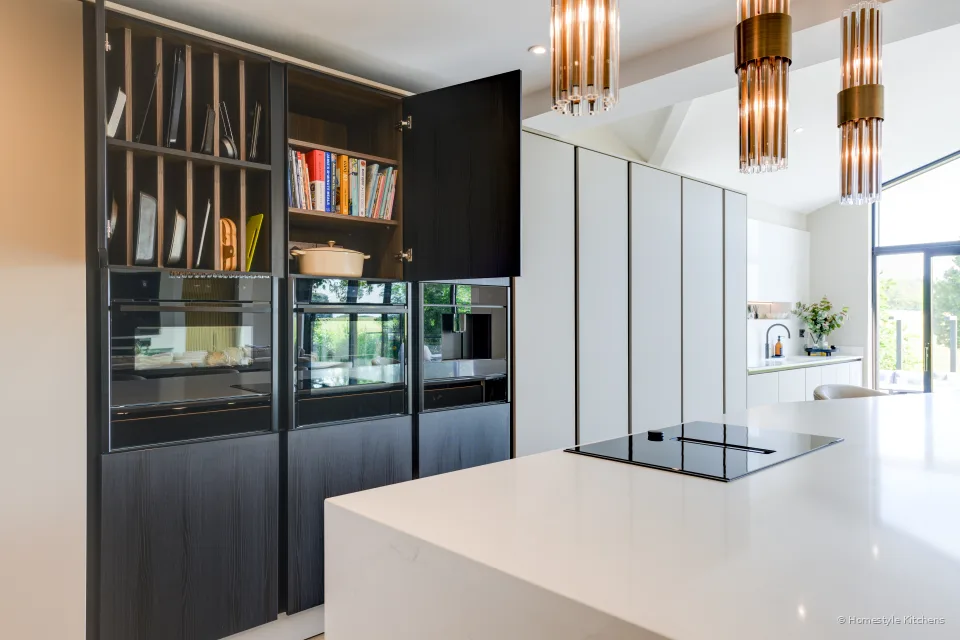 Dark glazed tall cabinetry with integrated appliances, herringbone oak floor.