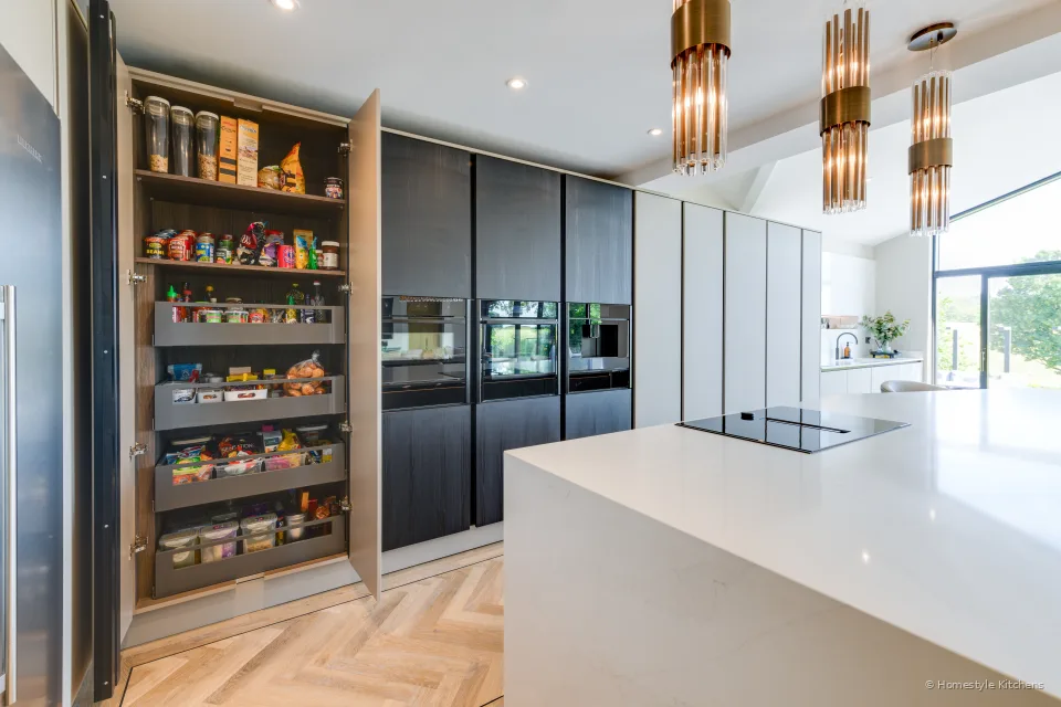 Tall pale handleless units and island, window light across herringbone oak.