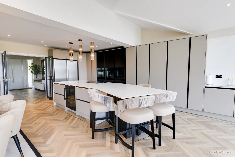 Dining table and pale kitchen island towards glazed doors, dark tall run beyond.