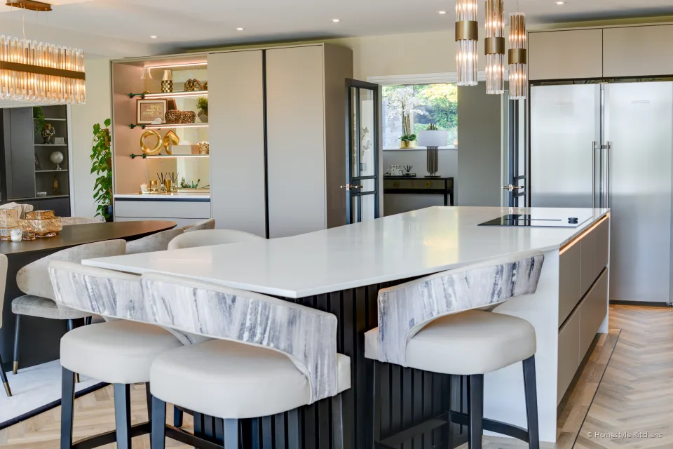 Upholstered stools at a pale grey island, brass pendants above.