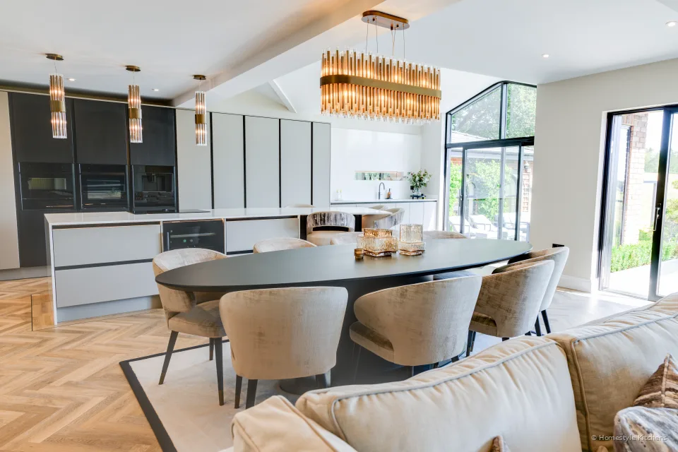 Dining table under brass pendants, dark cabinetry and pale island beyond.