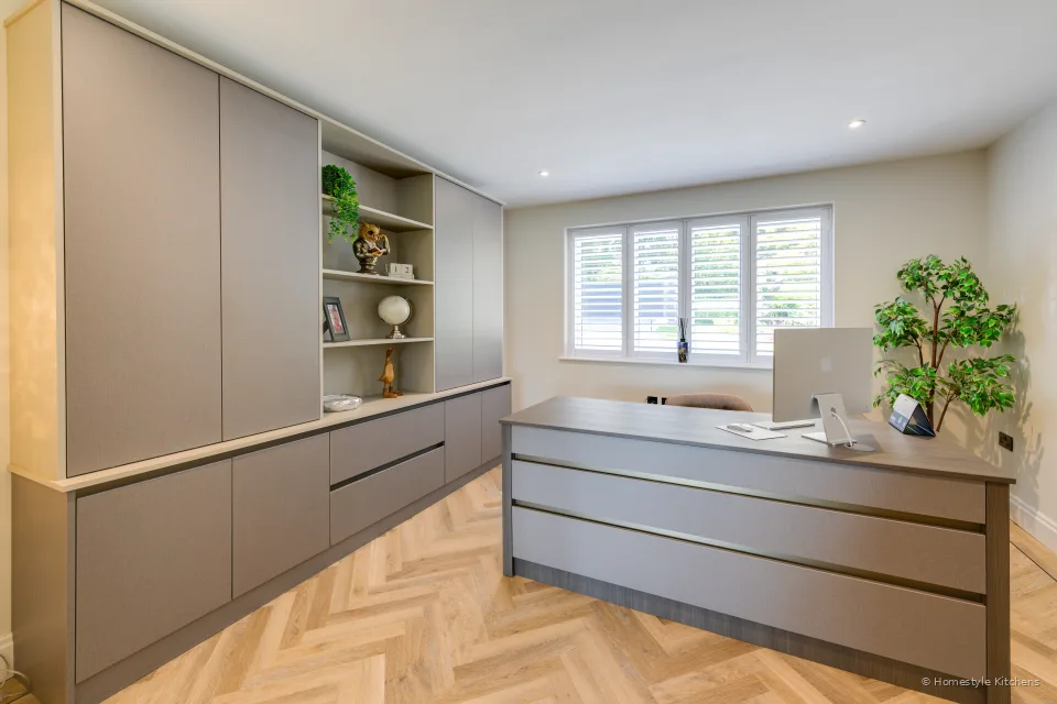 Taupe cabinetry with open shelving and a dark desk, herringbone oak floor.