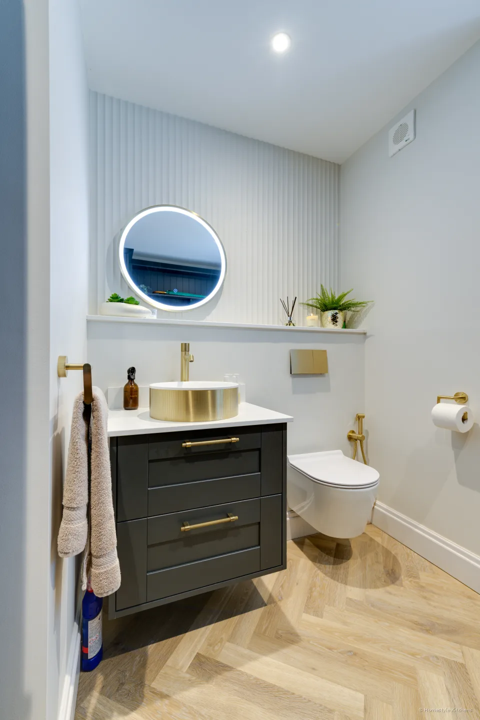 Dark green vanity with a brass basin and tap, round lit mirror.